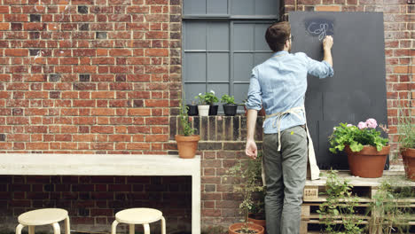 barista writing up chalk board outside cafe