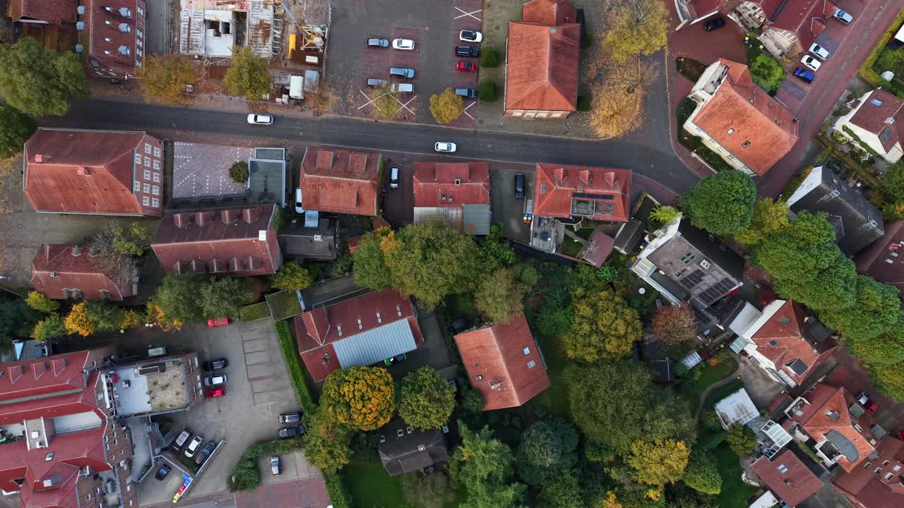 Driving cars on street of historic houses and homes with orange tile roof in German city. Colored trees in fall season. Aerial top down tracking shot