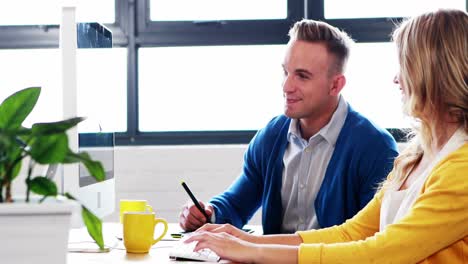 Businesswoman-interacting-with-man-while-working-on-computer