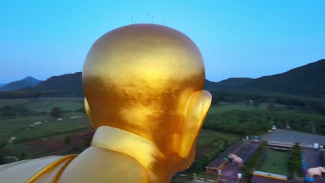 4k aerial face detail shot of a biggest luang pu thuat statue in the world surrounded by mountains of khao yai at dawn in thailand