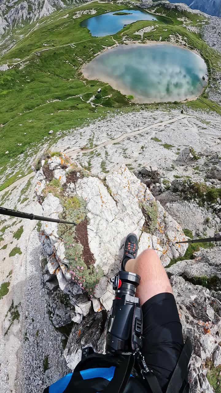 Camera reveals hiker's legs on rocky edge, framing Lago dei Piani below