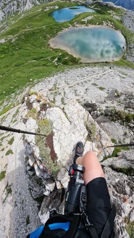 camera reveals hiker's legs on rocky edge, framing lago dei piani below