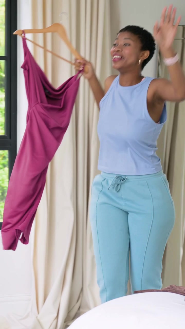 Vídeo vertical: Levantando um vestido bordô no cabide, mulher de azul caminhando até o espelho em casa analisando o caimento.