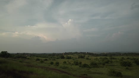 Timelapse-static-wide-shot-of-a-beautiful-landscape-during-a-sunset-with-the-clouds-quickly-passing-by-overlooking-a-green-field-with-bushes-and-plants-in-nature