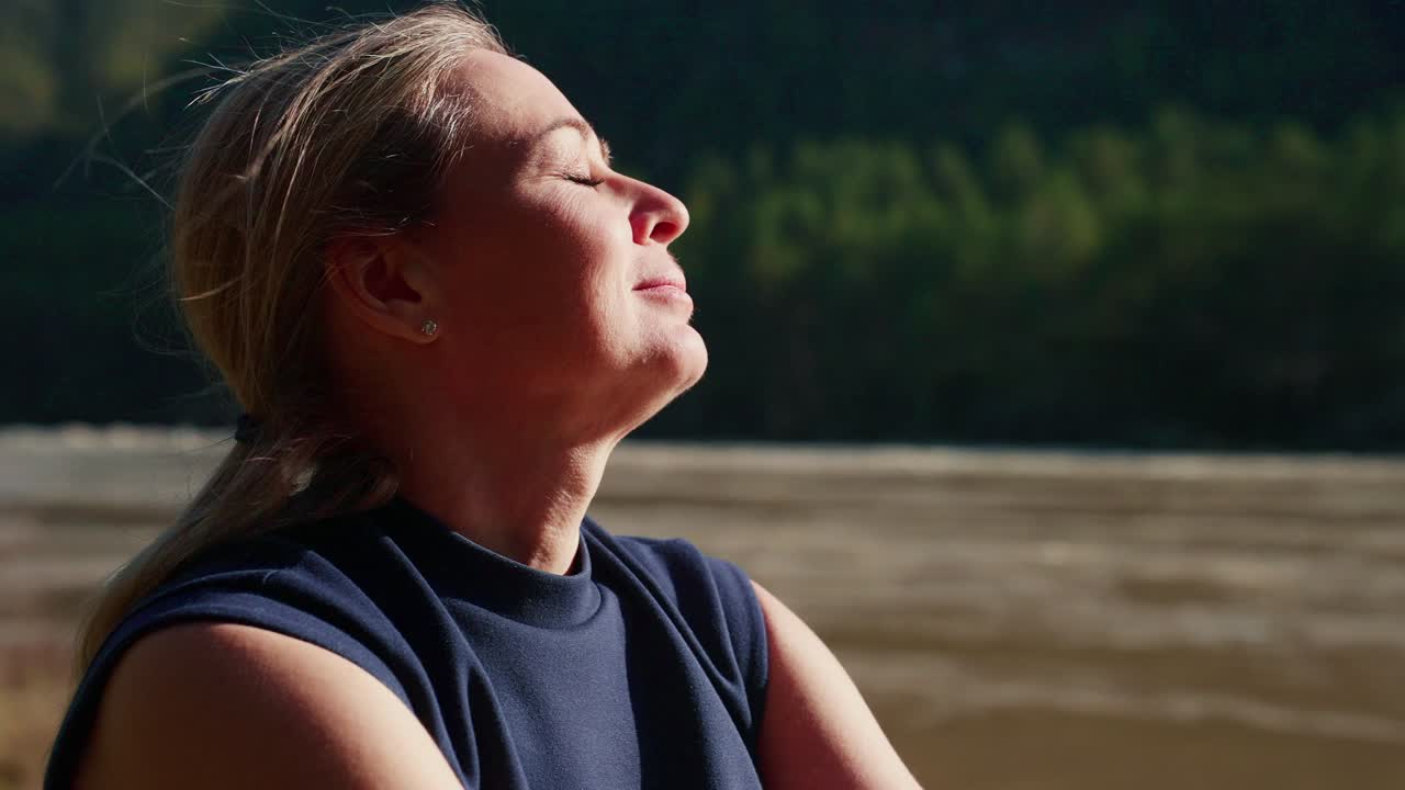 Mulher respira profundamente junto ao rio, com os olhos fechados, calma e serena. A luz do sol aquece sua pele, um momento pacífico na natureza. Perfeito para conteúdo de bem-estar, meditação ou viagens. Adequado para saúde, estilo de vida.