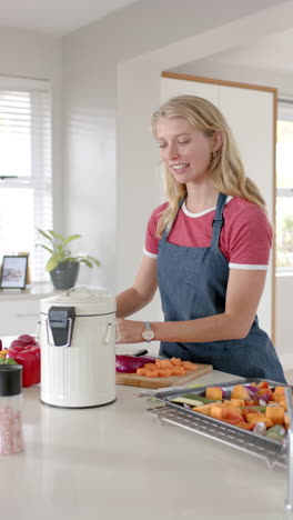 vertical video of happy caucasian woman throwing waste out in kitchen, slow motion