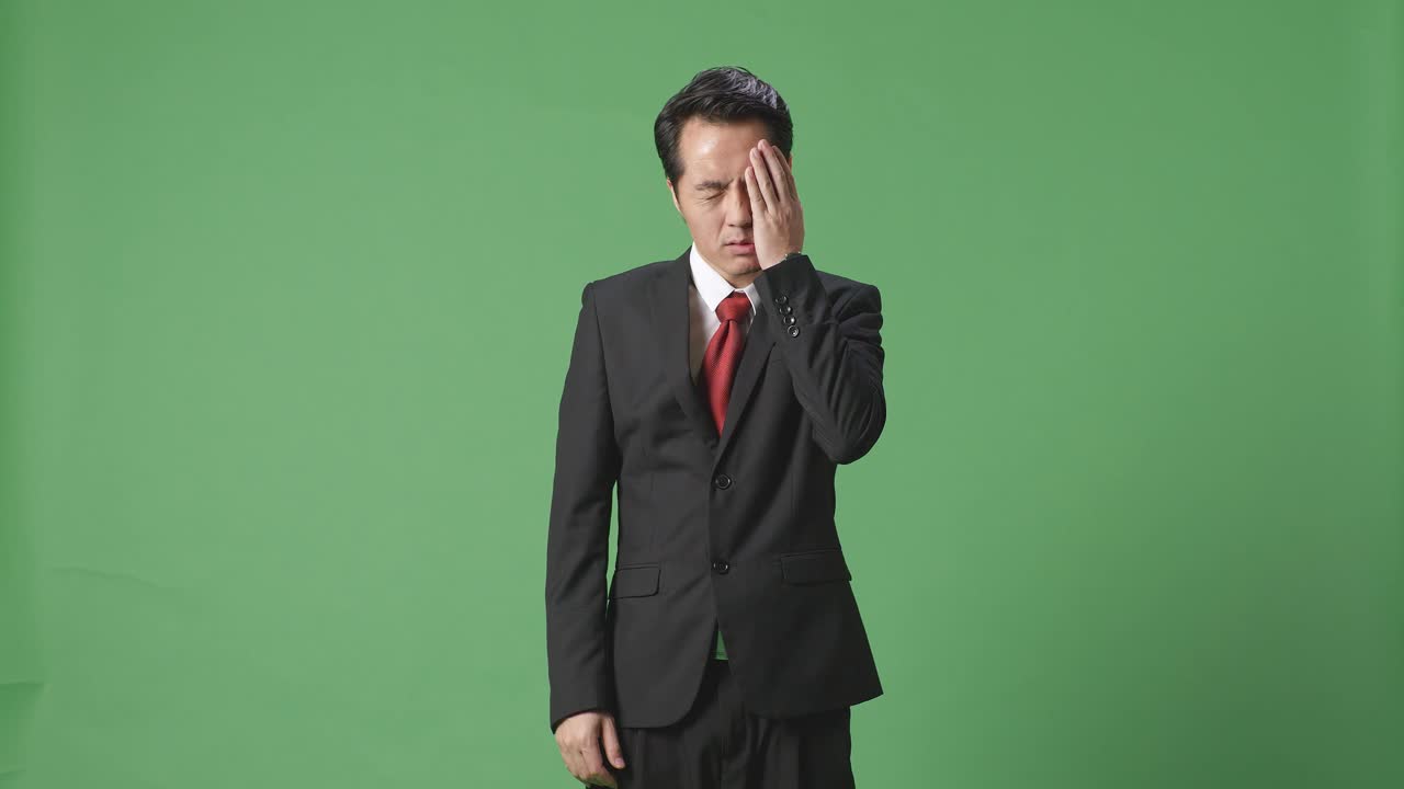 녹색 화면 앞에 서 있는 피곤한 아시아 사업가