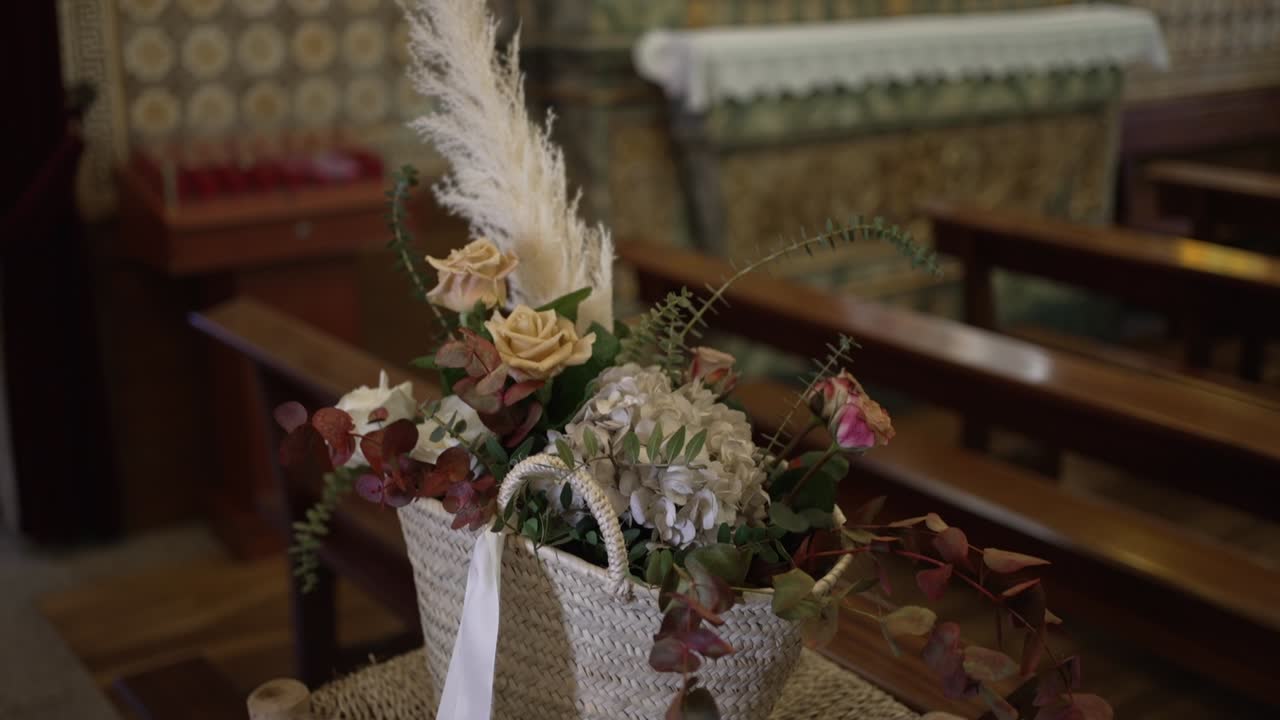 cesta rústica con flores, vegetación y hierba de pampas colocada en un soporte dentro de una iglesia