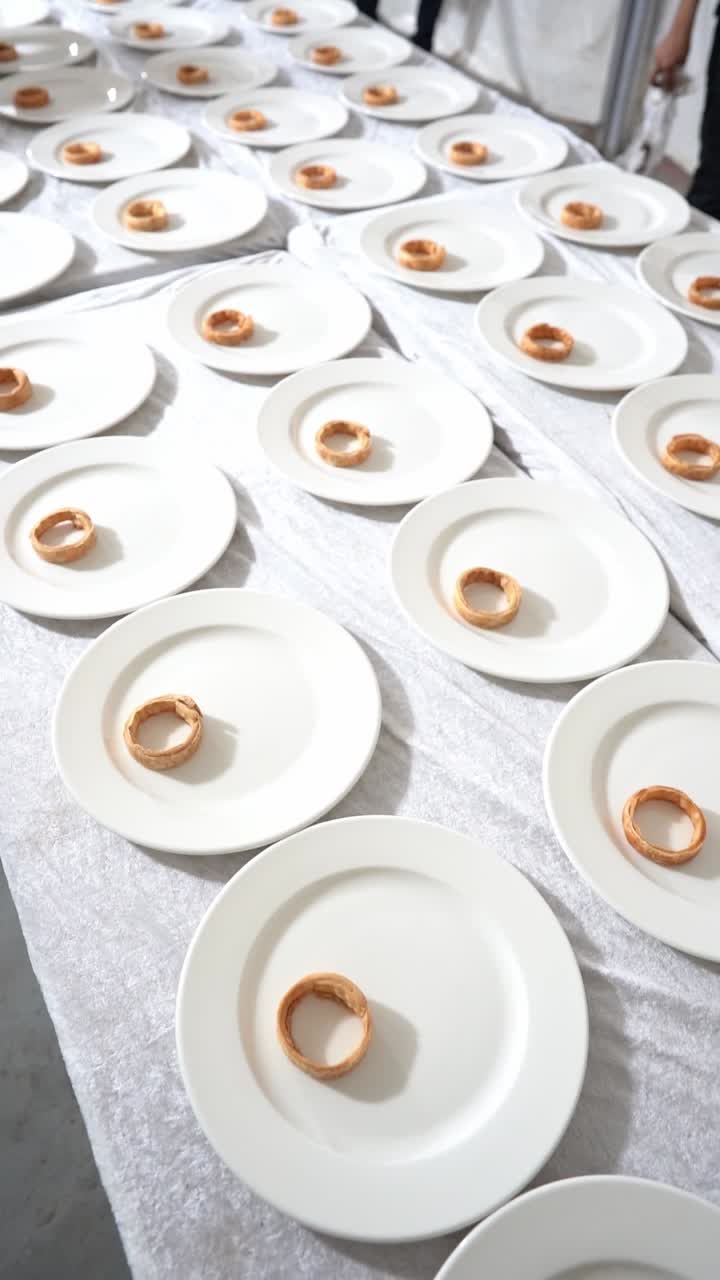 Minimalist fine dining setup with white plates arranged in rows, each holding a small pastry, close up shot