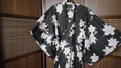 Schwarz-weißer-Kimono-Mit-Blumenmuster,-Der-In-Einem-Faltbaren-Raumteiler-Aus-Holz-Aufgehängt-Ist