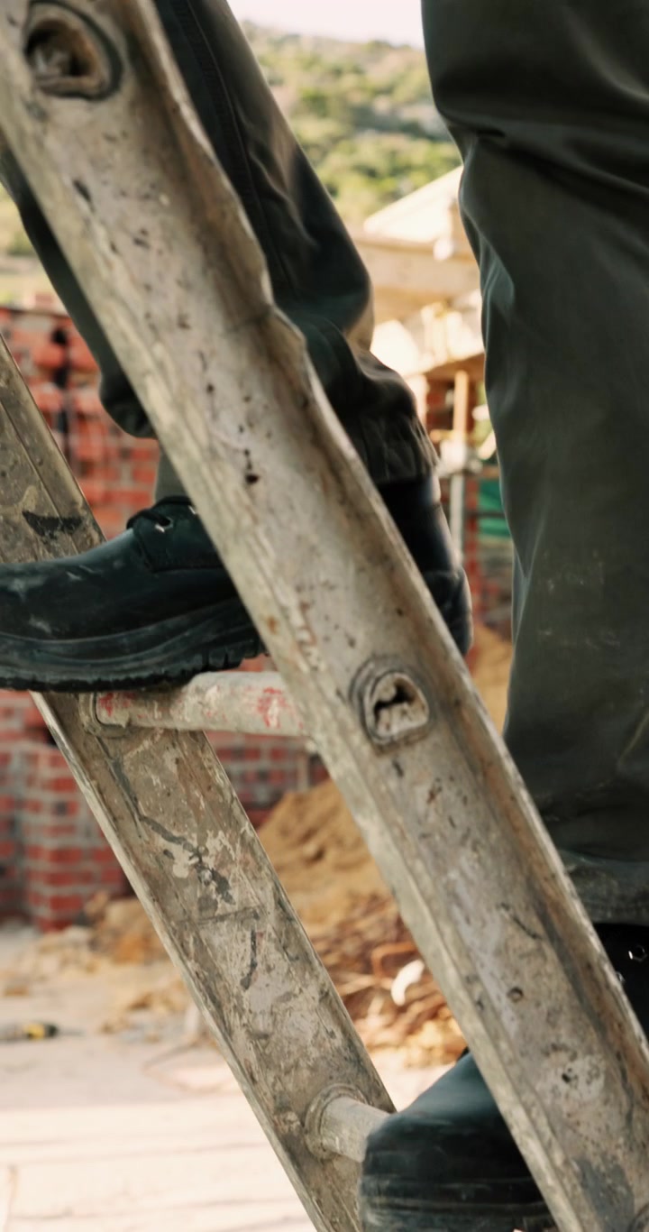 Construction Worker Climbing Up a Wooden Ladder at a Building Site