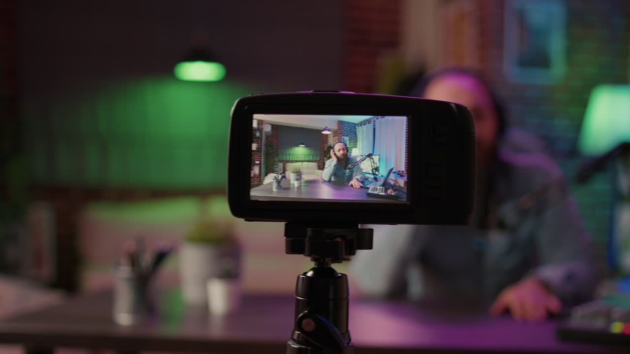Selective focus on digital video camera screen recording male vlogger with headphones talking at microphone