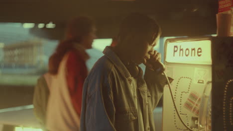 black man speaking at phone booth on street under overpass in evening