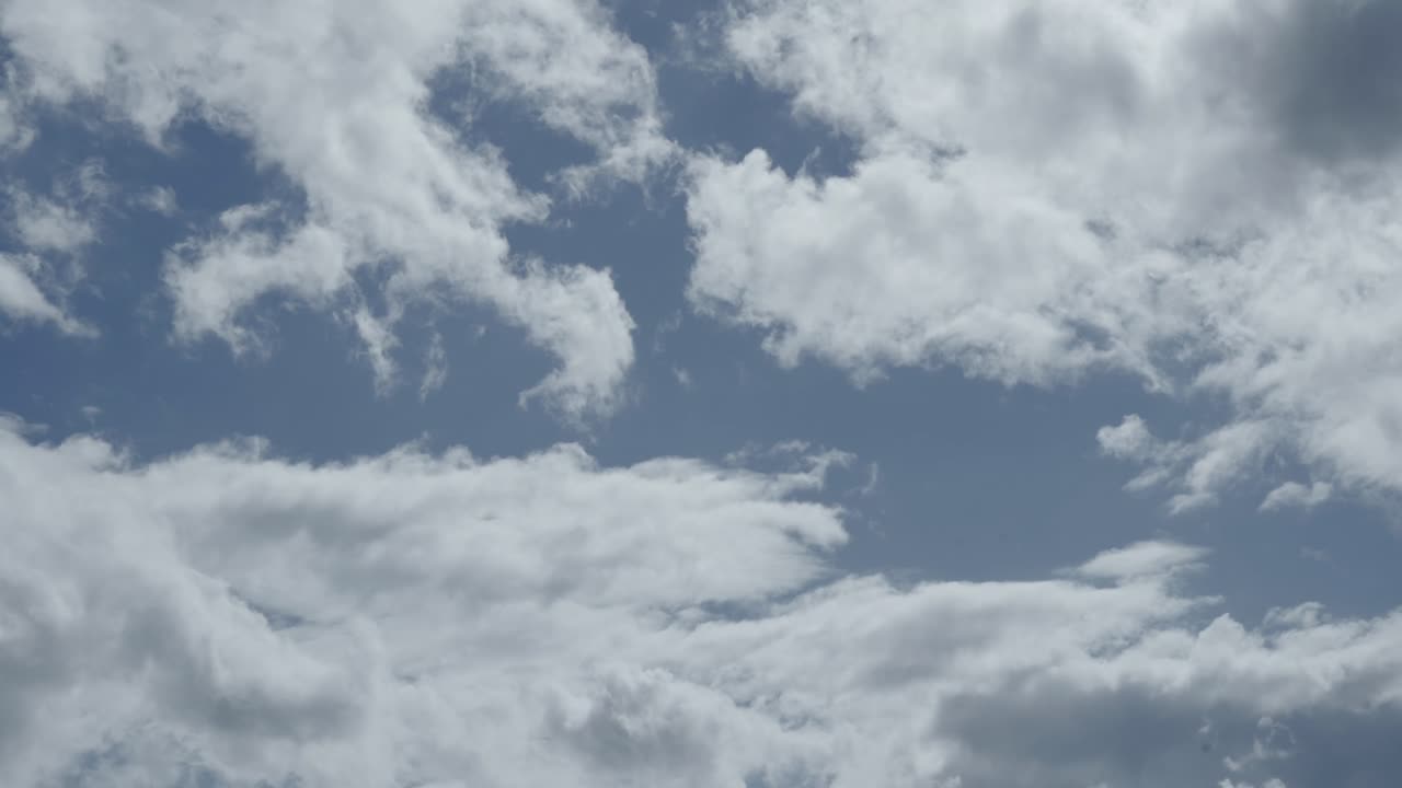 Fluffy white clouds move slowly across a blue sky, creating a calm and open atmospheric scene