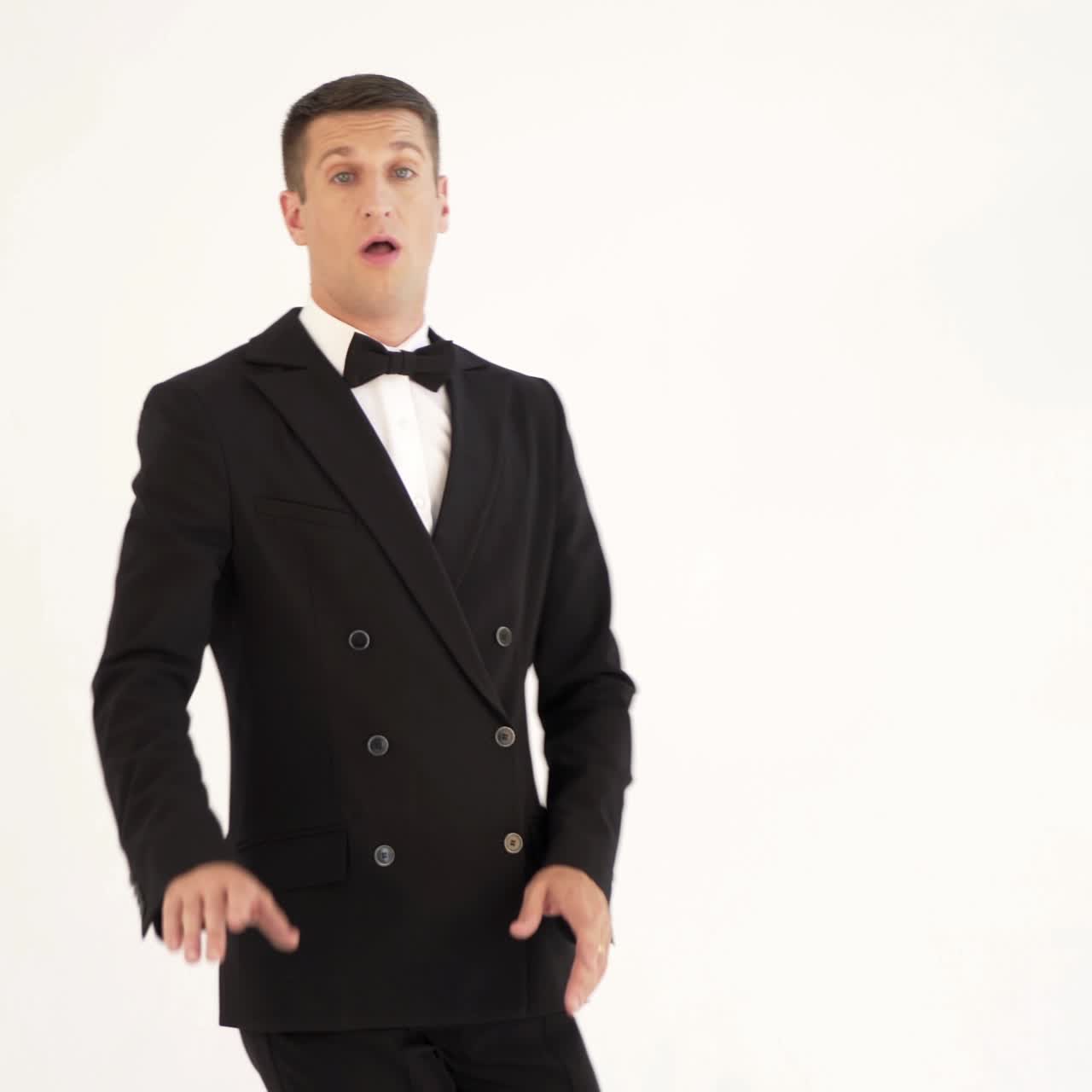 a showman in a stylish black suit with a bow tie is posing and walks out of sight on the white background.