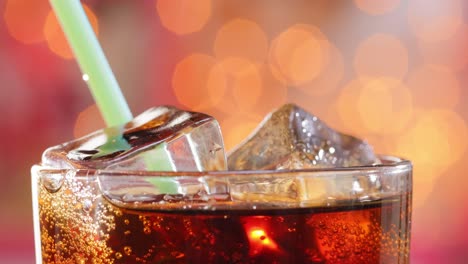 y beber un tubo de cola con hielo y burbujas en vidrio en una luz borrosa, fondo borroso.