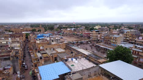 Antenne-Fliegt-über-Dächer-In-Der-Stadt-Jaisalmer-In-Richtung-Indische-Flagge,-Die-Im-Wind-Auf-Der-Stange-Flattert