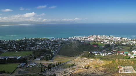 Toma-Panorámica-De-La-Ciudad-Costera-Junto-A-La-Bahía,-Vista-Aérea-Desde-La-Montaña,-Hermanus,-Sudáfrica