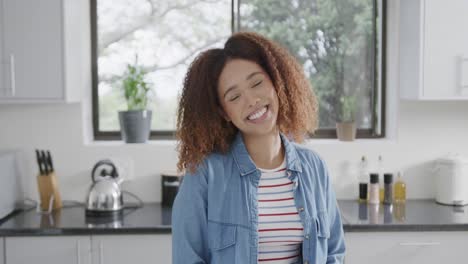 Portrait-of-happy-biracial-woman-with-curly-hair-smiling-in-kitchen,-slow-motion