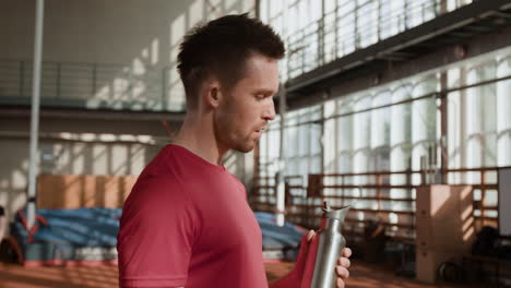 man drinks water from bottle during workout break in gym