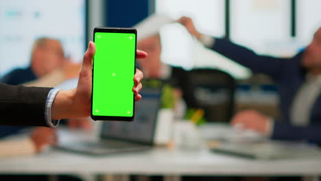 businesswoman holding smartphone with green screen during conference