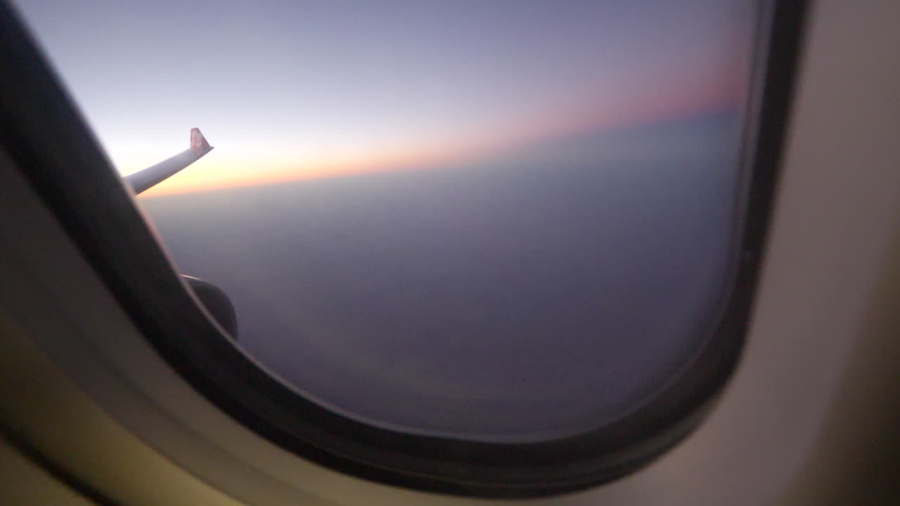 A view from the window seat of an airplane during sunset above the clouds.