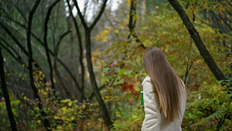 happy active smiling woman walks in the park with paper cup in her hand. lady walking looking into camera and waving her hand. autumn nature backdrop.