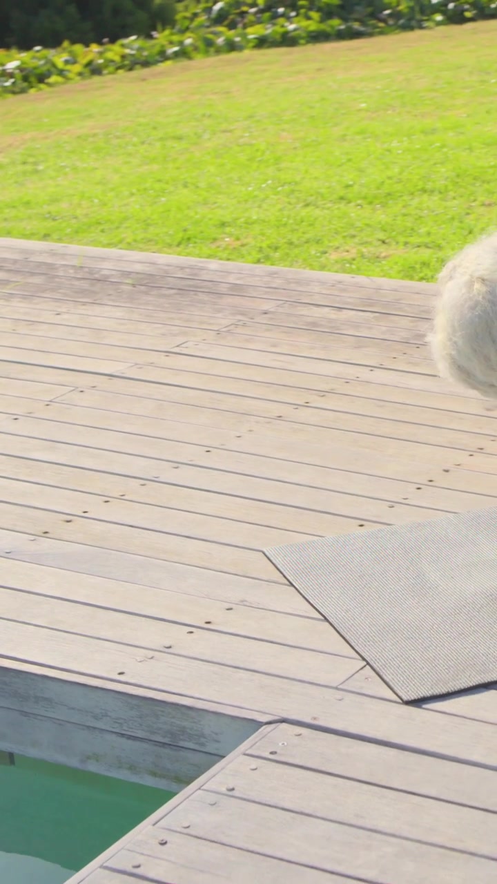 Vertical video: Bending woman in pink top leggings leaning into deck gap checking, showing yoga mat