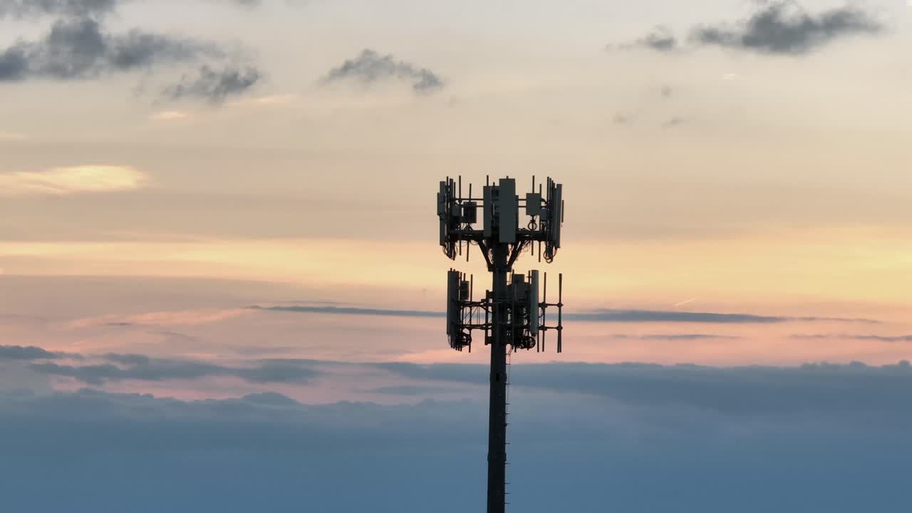 Silhouette of cell tower over cloudscapes and sunset light. Aerial orbit shot. Telecommunication tower or radio mast in America