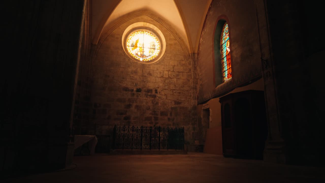 Vista interior do teto abobadado de pedra e dos vitrais coloridos de um edifício religioso em Issigeac. Perspectiva de baixo ângulo.