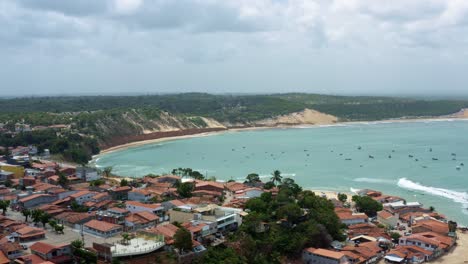 truck left aerial drone wide shot flying over homes to the famous baia formosa beach in the state of rio grande do norte, brazil with fishing boats, coastal homes, and small waves on a summer day