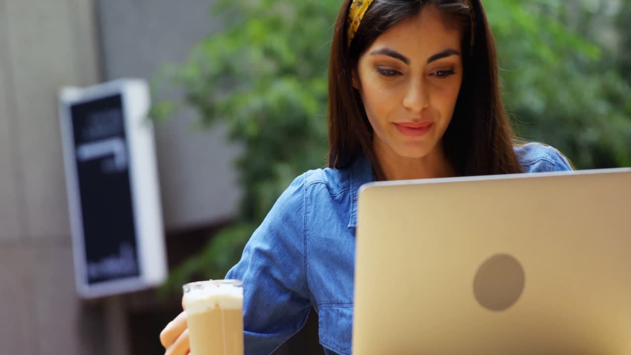mujer tomando un batido mientras usa una computadora portátil en un café al aire libre 4k
