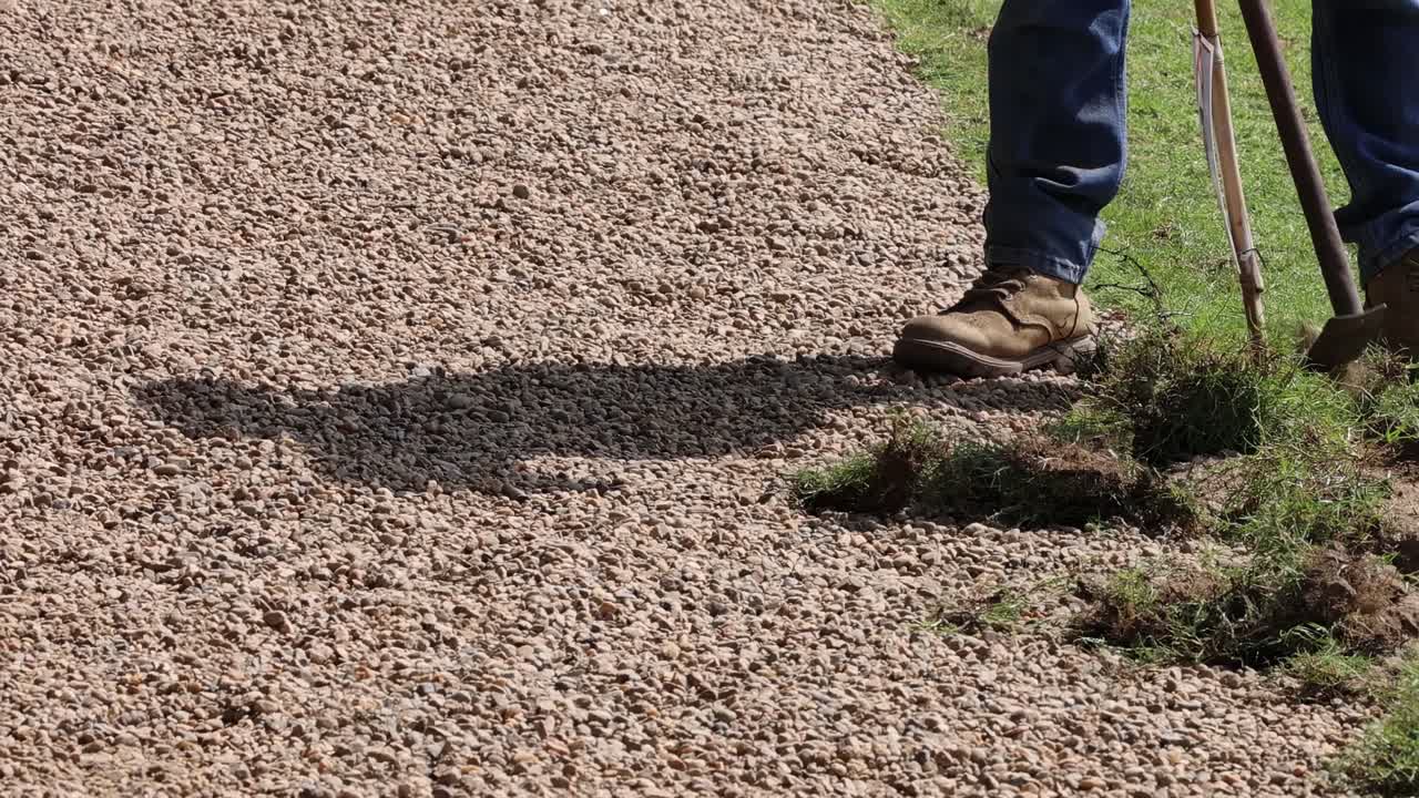 Close-up of boots on gravel path beside grass clippings and green lawn.