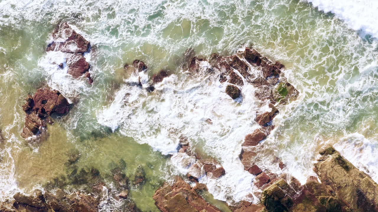Waves rolling from right corner of frame onto sedimentary ocean rocks ...