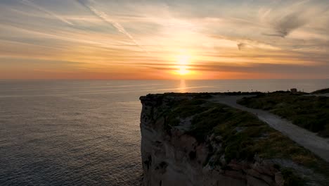 spectacular drone shot of migra l-ferha’s limestone cliffs at sunset, with golden light reflecting across the calm mediterranean sea and dramatic coastal landscape.