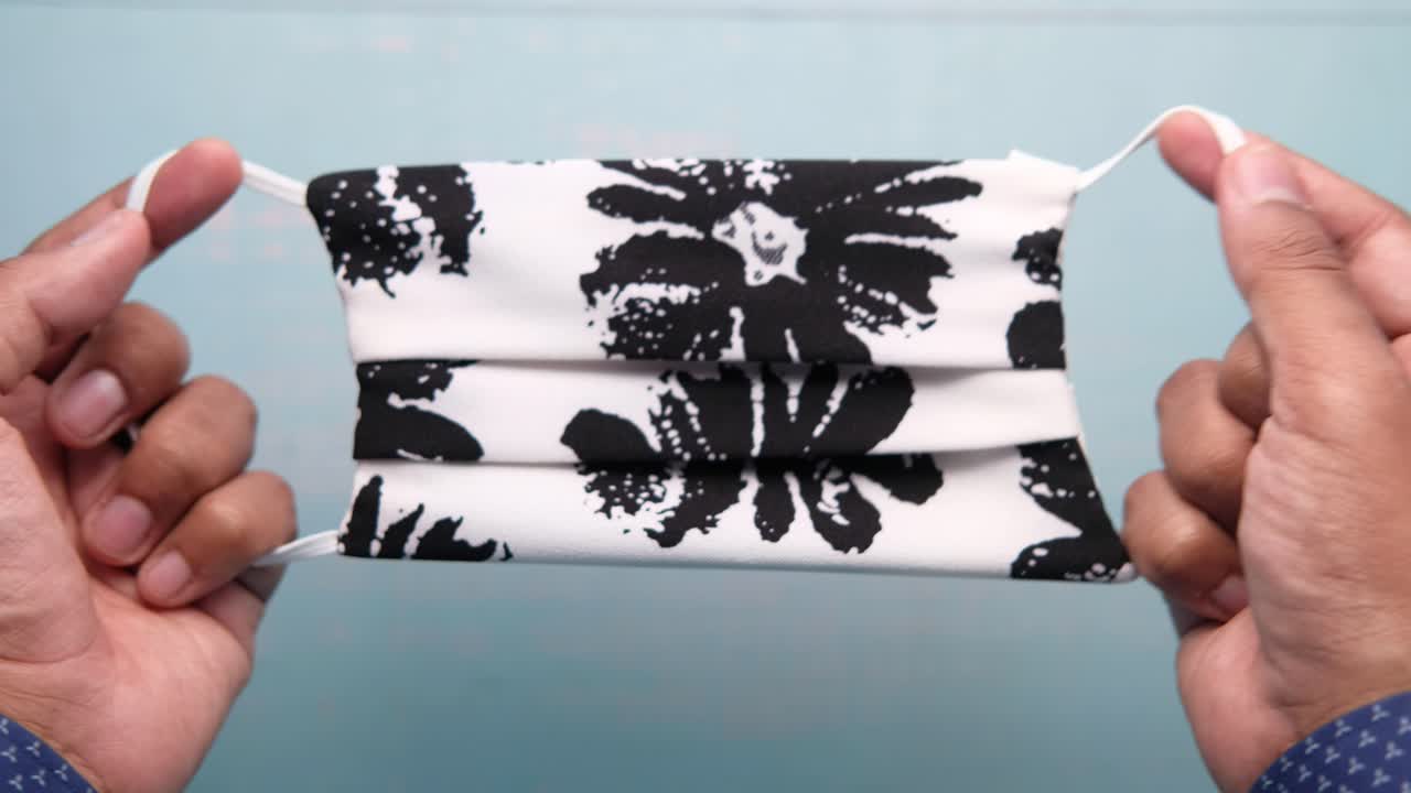 인쇄 된 직물 얼굴 마스크 를 들고 있는 사람