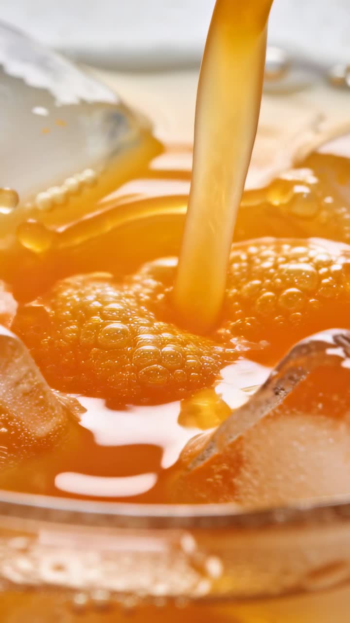 Video verticale: Liquido ambrato che si versa sul ghiaccio, formando uno schizzo a corona e bollicine, per promuovere una bevanda.