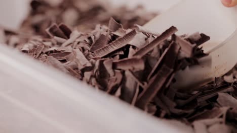 baker chef grabs vegan tasty chocolate pieces with plastic scoop inside food container close-up shoot