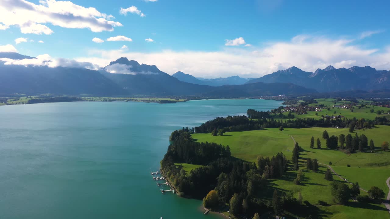 impresionante vista aérea volando lateralmente sobre un enorme lago con vistas a los alpes con una impresionante cordillera en forggensee en baviera, alemania en 4k