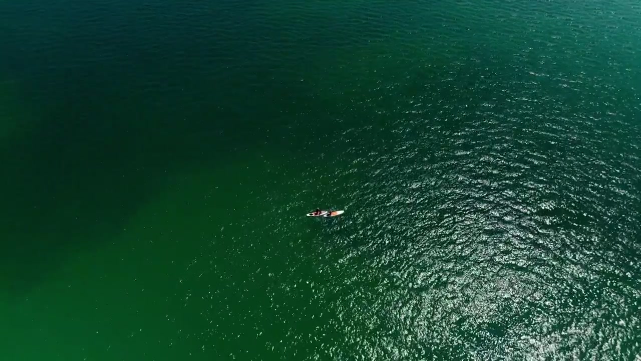 Aerial drone View of paddleboarders moving across calm green sea near West Bay Beach in Dorset England showing expansive water surface and coastal recreation