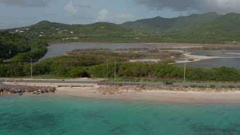 Aerial-tracking-view-4wd-vehicle-drive-on-Antigua-and-Bermuda-coast-with-blue-turquoise-waters-and-sandy-beach