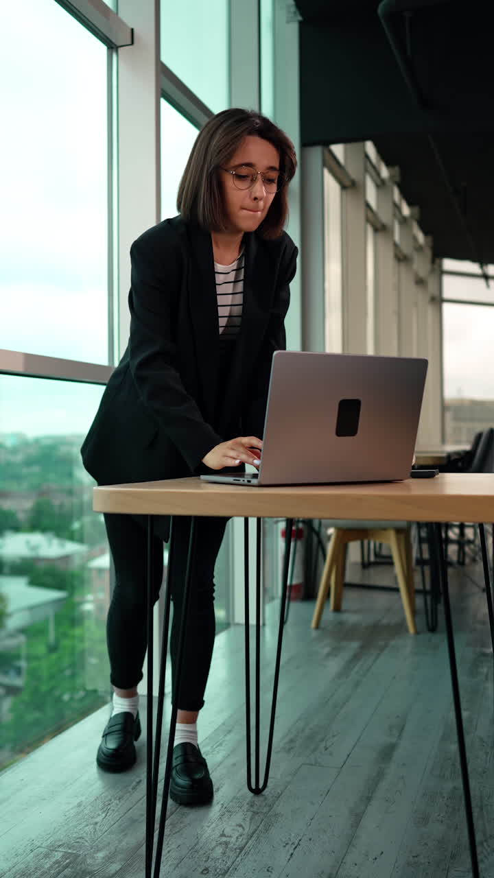Pensive woman looking at the window puts on her glasses. Business lady turns to computer and starts her work. Low angle view. Vertical video.