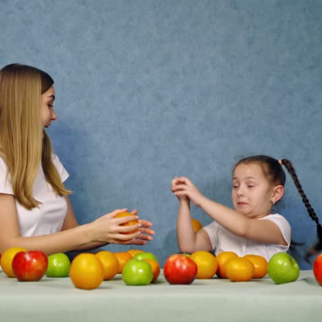 woman and little girl with healthy fruit. happy mother and daughter in white t-shirts playing with fresh organic fruits on blue background.