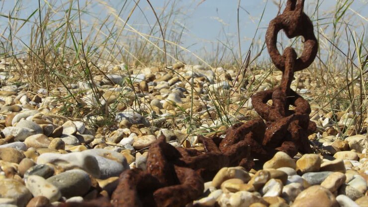Rusty chain swinging in the wind on the pebble beach