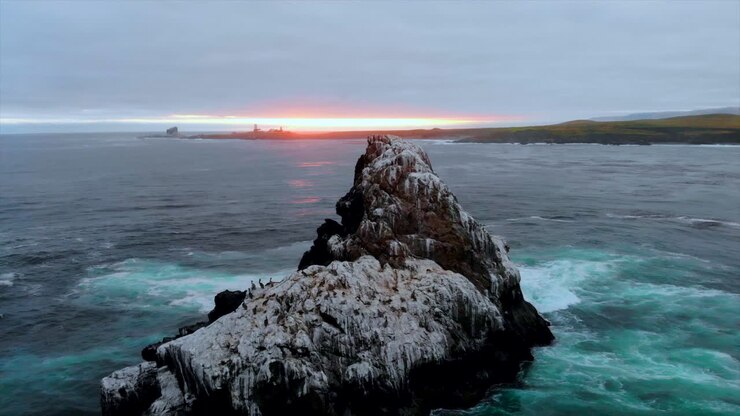 Sorvolo con drone della Roccia della colonia di uccelli e vista su un magnifico tramonto sull'Oceano Pacifico e sul Faro di Piedras Blancas in lontananza, con le onde impetuose dell'Oceano Pacifico vicino alla Highway 1, Hearst Castle, 4k Pro Res 422 HQ