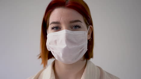 Portrait-of-woman-with-heart-shaped-hands-winking-and-wearing-medical-face-mask-and-gloves,-looking-at-camera.-Close-up.-Frontal-view