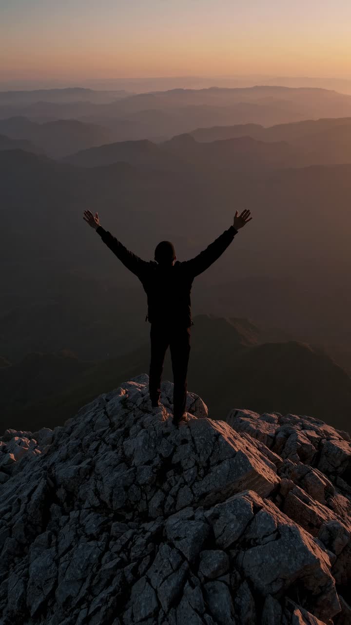 Silhouette of a person on a mountain peak at sunset, arms raised