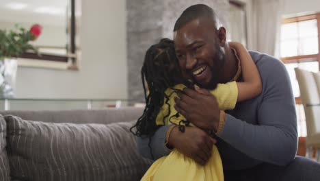 happy african american daughter and father hugging on sofa