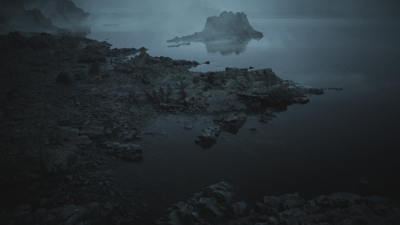 Misty shoreline view with rocky island at dawn near calm water body