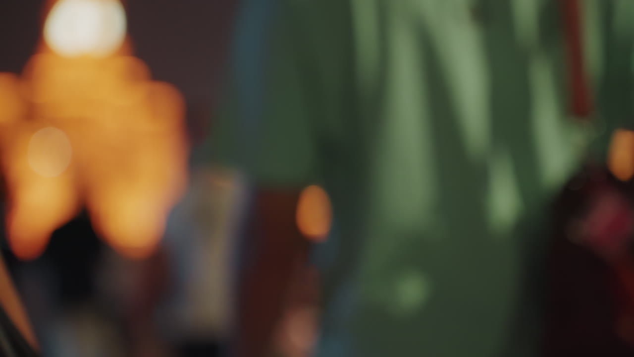Sagome sfocate di turisti e amici che camminano in città di notte, ripresi da dietro con messa a fuoco ridotta, luci al neon e lampioni caldi creano un bokeh morbido, abbigliamento estivo casual, borse a tracolla, passo lento